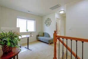 Ein Zimmer mit Treppe, einem Fenster mit Jalousien, einer Couch, einem Tisch mit Pflanze und einer Wanddekoration.