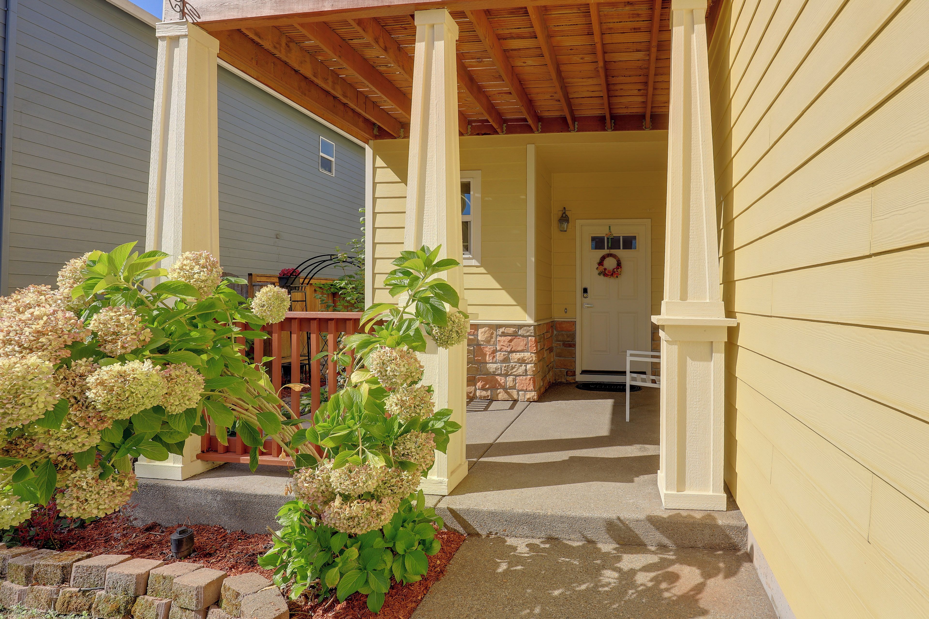 A covered porch with a wooden railing, a door with a wreath, and a small garden with hydrangea plants.