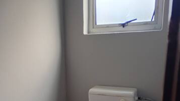 A small, basic bathroom with a toilet, a window, and a wall.