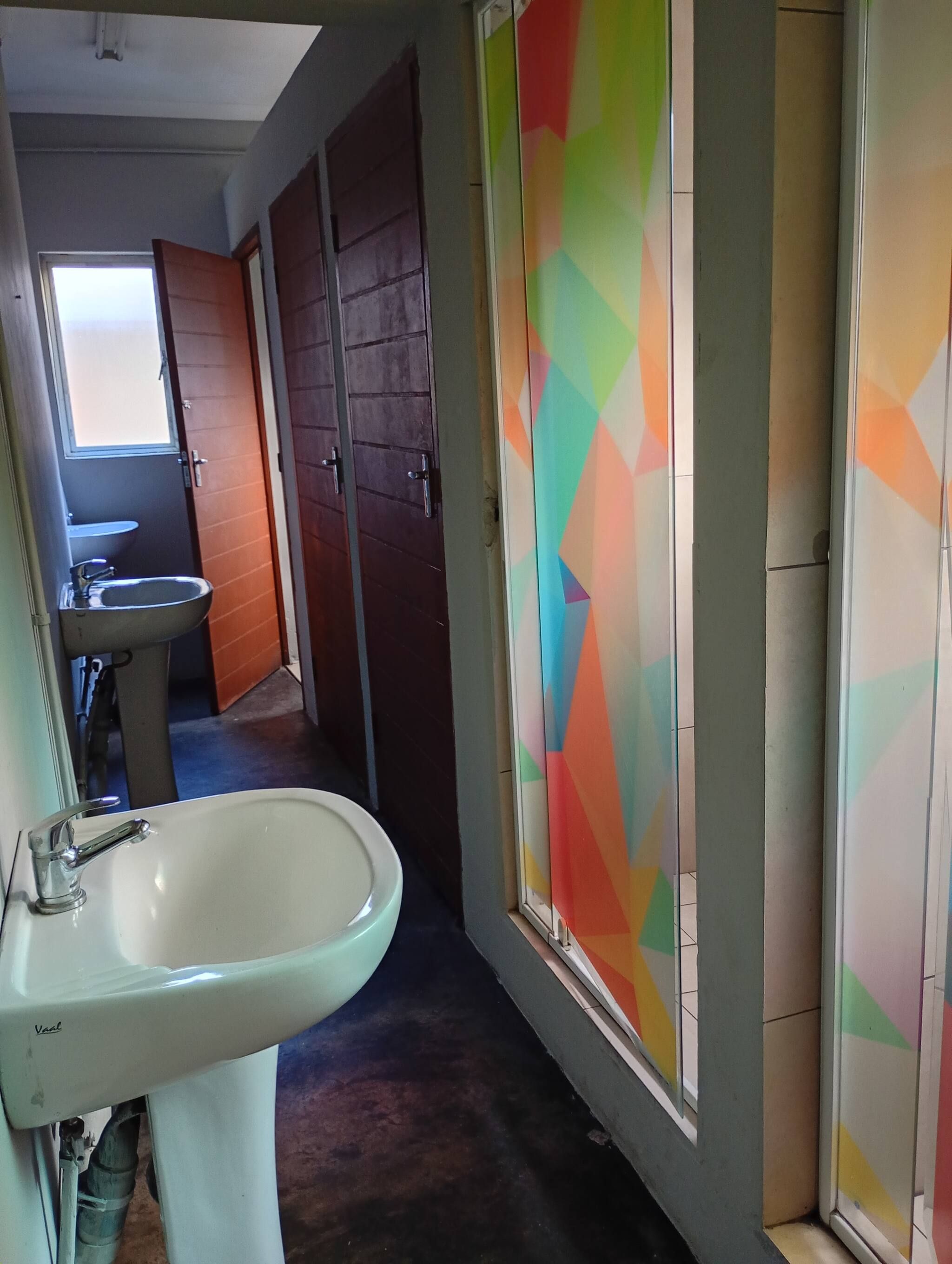 A narrow hallway with a white sink and a window with colorful geometric patterns.