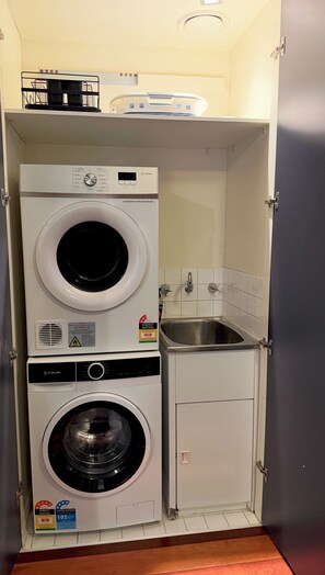 A compact laundry room with two stacked washing machines, a small sink, and a cabinet. - Monroe X Banksy Loft | Luxury CBD Stay| Pool & Gym (Melbourne)