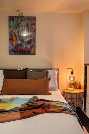 A bedroom with a bed, pillows, a blanket, a wall-mounted artwork, a bedside lamp, and a small table with a plant. - Monroe X Banksy Loft | Luxury CBD Stay| Pool & Gym (Melbourne)