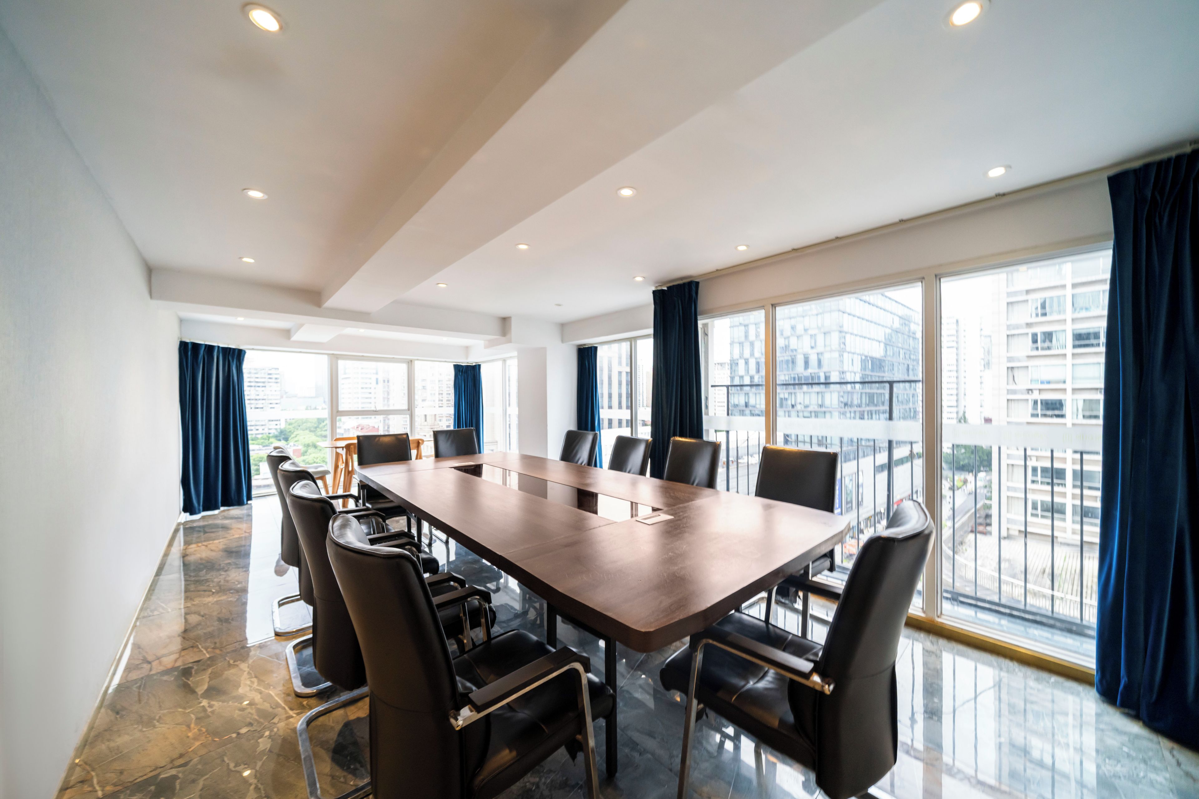 A conference room with a long table, chairs, and large windows with curtains.