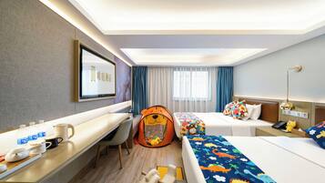 Een hotelkamer met een bureau, twee bedden, een kinderspeeltent en een bureaulamp.