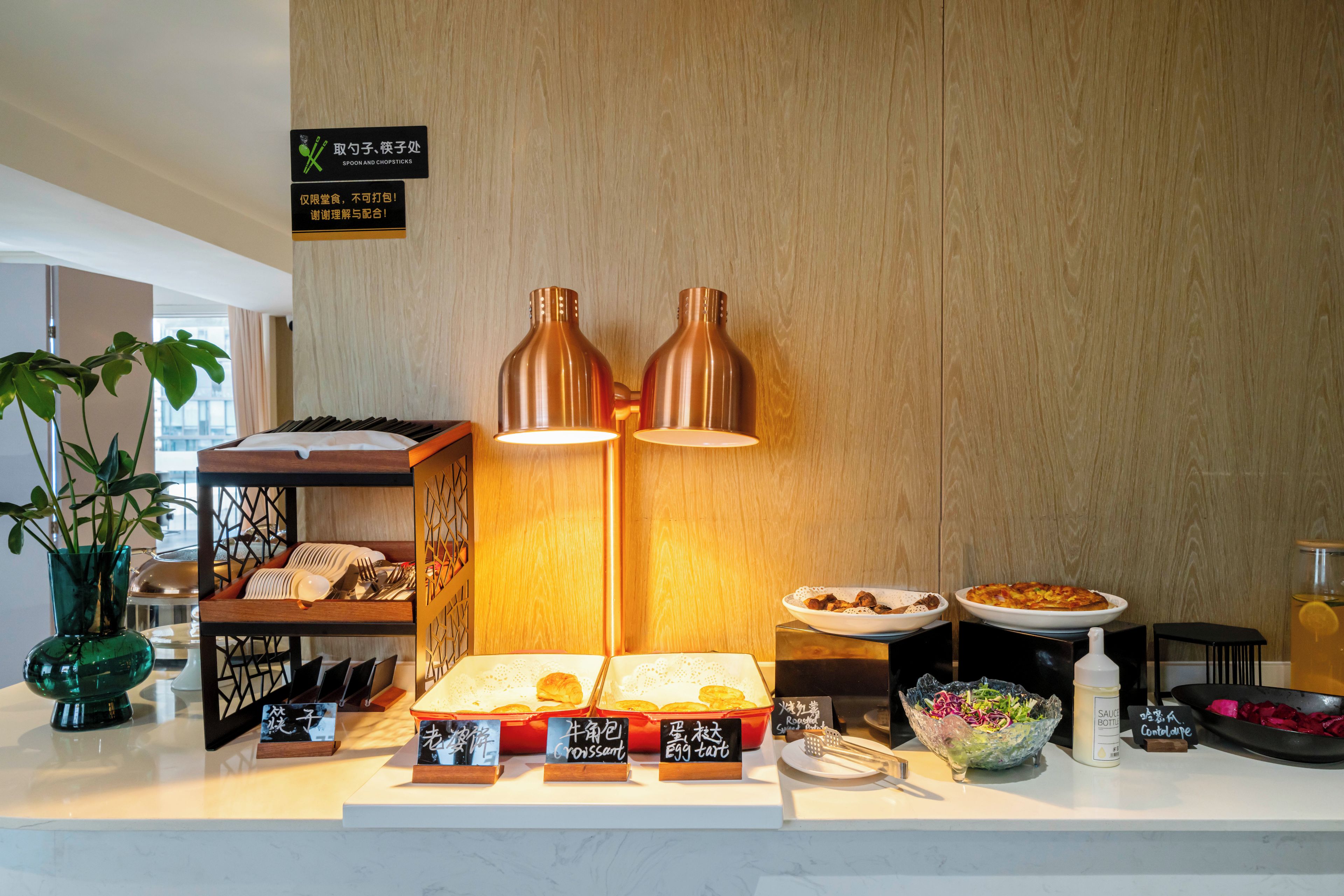 A breakfast buffet with labeled food items and a sign indicating the use of utensils.