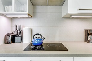 A kitchen with a black induction cooktop, a blue kettle, and various utensils. - Boardwalk Escape: Beachfront Santa Monica Condo (Santa Monica)