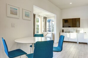 Uma sala de jantar moderna com uma mesa redonda e cadeiras azuis, um sofá e uma TV fixada na parede.