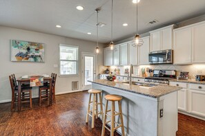 A modern kitchen with white cabinets, a granite countertop, a built-in microwave, and a stainless steel stove. There are two wooden stools at the island, and a painting hangs on the wall. - Hot Tub & Patio! Family Escape, 7 Mi to SeaWorld (San Antonio)