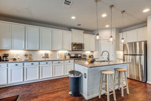 Une cuisine moderne avec des meubles blancs, des appareils en acier inoxydable et un îlot central doté de tabourets.