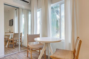 A room with a round table and two wicker chairs, a television on the wall, and a large window with curtains. - Sunset Strolls & Seaside Fun: Santa Monica Condo! (Santa Monica)