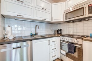 A modern kitchen with stainless steel appliances, white cabinetry, and a tiled backsplash. - Sunset Strolls & Seaside Fun: Santa Monica Condo! (Santa Monica)