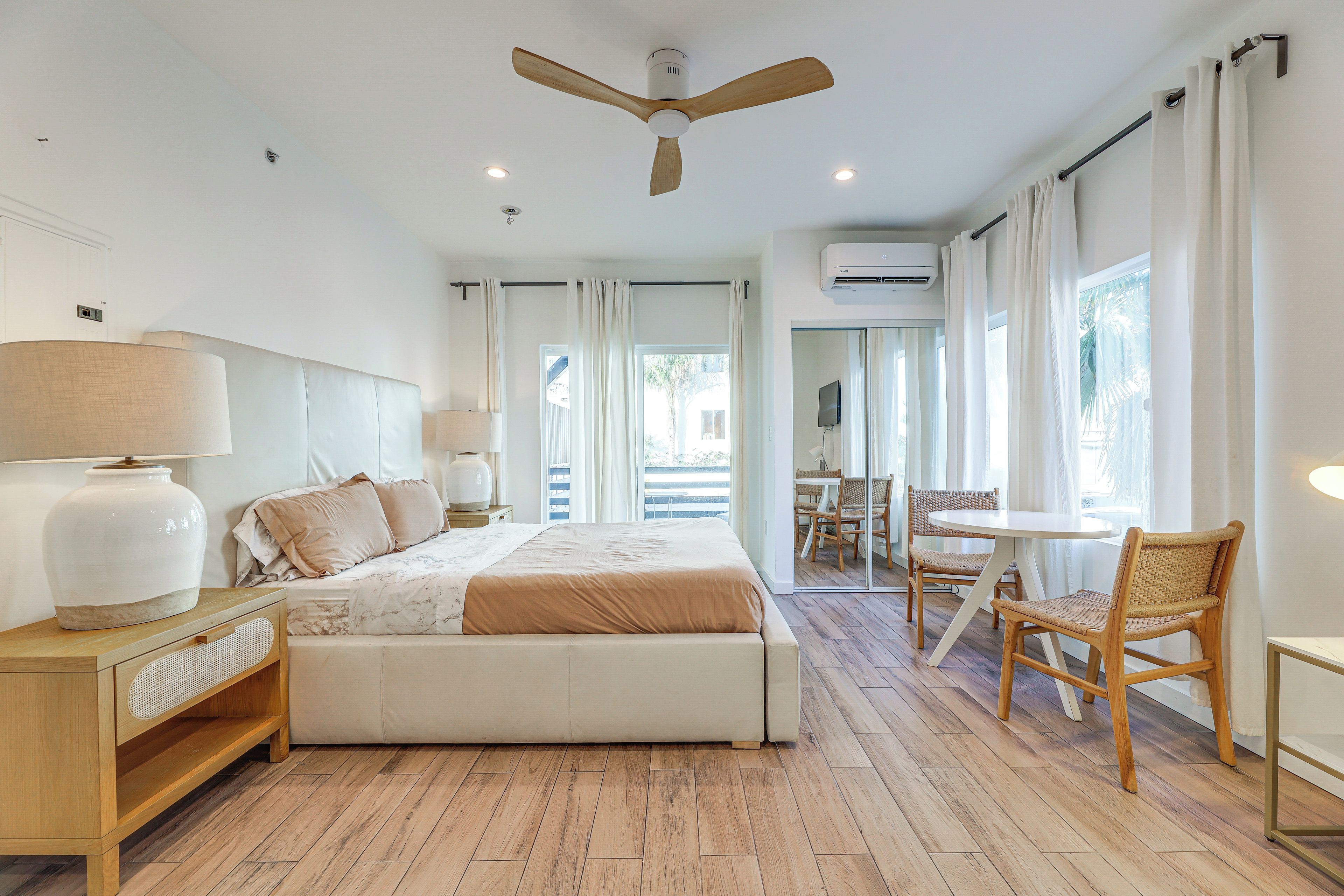 A bedroom with a bed, bedside tables, a ceiling fan, and a view of the outside.