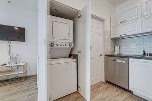 A compact kitchen with white cabinetry, a built-in washer and dryer, and a dishwasher. - Sunset Strolls & Seaside Fun: Santa Monica Condo! (Santa Monica)