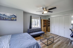 Ein Schlafzimmer mit Bett, Sofa, Deckenventilator, Fenster mit Vorhängen, Kleiderschrank und einem Bild an der Wand.