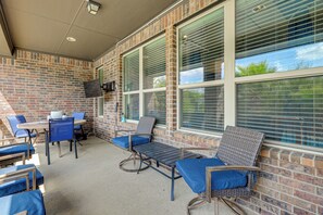 A covered outdoor seating area with brick walls, large windows, and a flat-screen TV mounted on the wall. - Home Theater & Game Room! 7BR San Antonio Retreat (San Antonio)