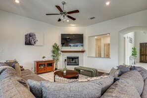 A living room with a ceiling fan, a fireplace, and a large window. - Home Theater & Game Room! 7BR San Antonio Retreat (San Antonio)