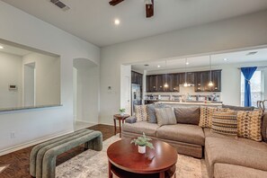 A spacious living room with a large sofa, a coffee table, and a bench. There is a kitchen visible through an open doorway. - Home Theater & Game Room! 7BR San Antonio Retreat (San Antonio)