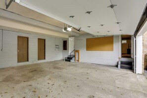 A spacious indoor area with a concrete floor, wooden doors, and a staircase leading to an upper level. - Youngstown Home Near Fellows Gardens & Lake Milton (Youngstown)