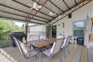 Ein überdachter Außenbereich mit Tisch, Stühlen, Grill und Deckenventilator.