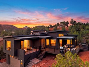 Une maison moderne à deux étages dotée d’une terrasse, d’un espace salon extérieur et offrant une vue sur le paysage environnant.