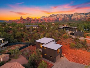 A modern house with a flat roof, surrounded by a desert landscape with red rock formations in the background. - Covered Lounge + Fire Pit + BBQ | Red Rock Views + Mins to Town | Casa Alta (Sedona)