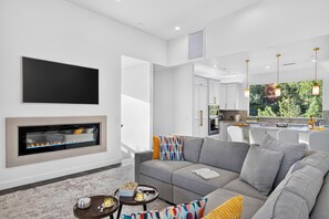 Ein modernes Wohnzimmer mit Kamin, großem Flachbildfernseher und einer Couch mit bunten Kissen.