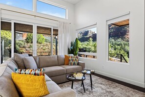 Un salon moderne avec un canapé d’angle, une table basse et de grandes fenêtres donnant sur un paysage montagneux.