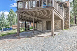 A covered outdoor area with a stone wall and wooden beams, surrounded by gravel and trees. - Comfortable Cabin w/ Hot Tub, Near Old Midtown (Ruidoso)