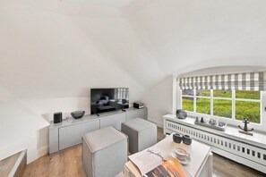 Ein modernes Wohnzimmer mit Fernseher, einer Couch, einem Couchtisch und einem Fenster mit Blick auf Grünflächen.