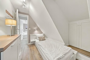 Un dormitorio compacto con techo inclinado, una mesita de noche con lámpara, cama con almohada y un armario.