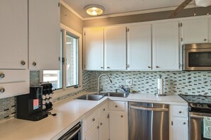 Eine moderne Küche mit weißen Schränken, einer Edelstahl-Spüle, einer eingebauten Mikrowelle und einer Kaffeemaschine.