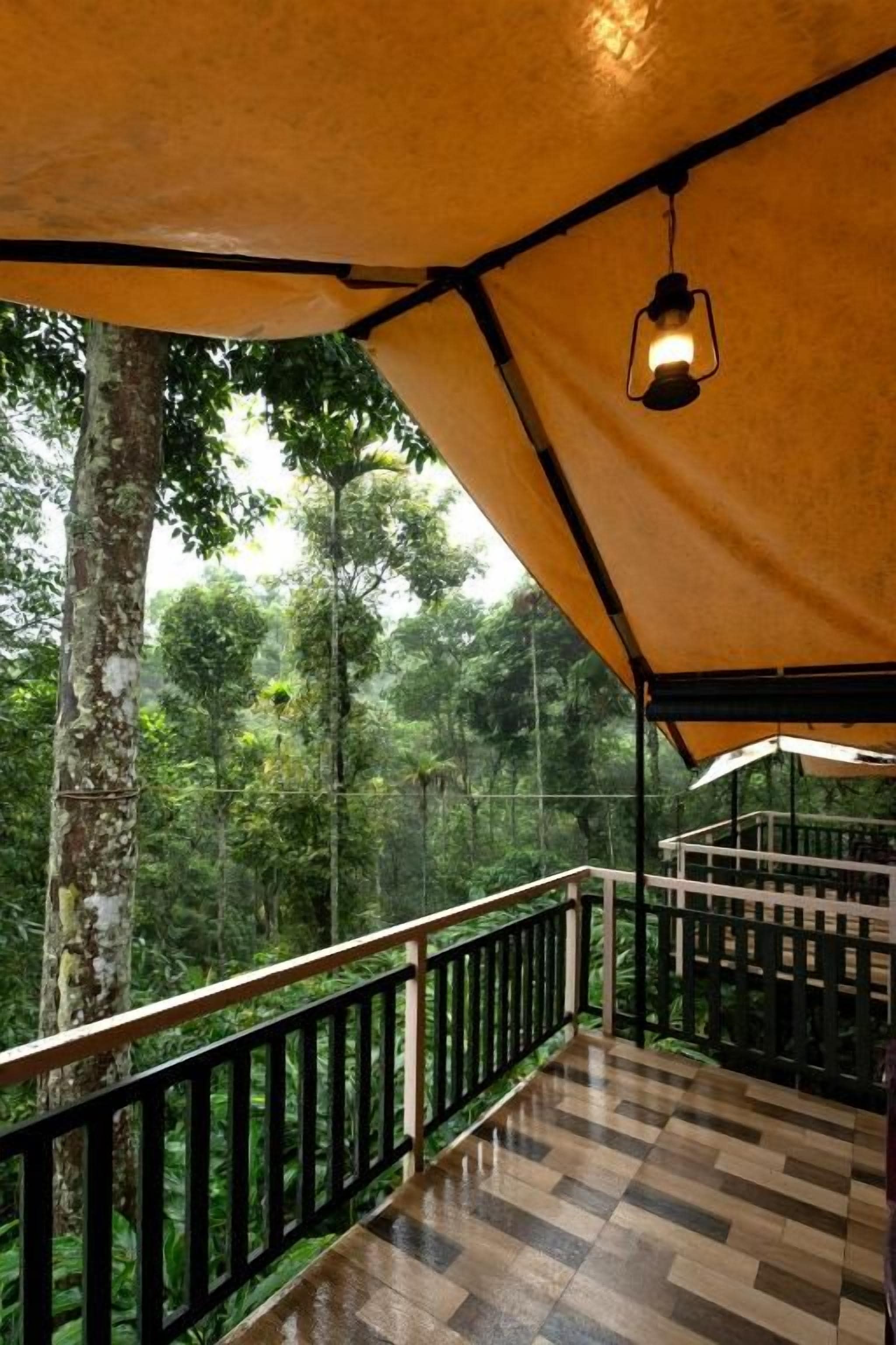 Un espacio al aire libre cubierto con suelo de madera y barandilla, rodeado de un bosque frondoso.