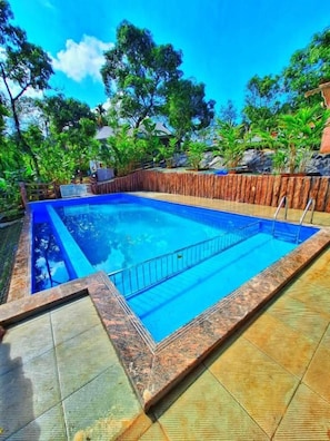 Una piscina rectangular con valla de madera y un borde de baldosas alrededor.