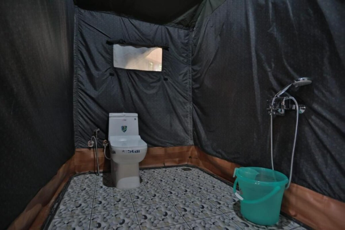 Un baño pequeño y cerrado con inodoro, ducha y un balde.
