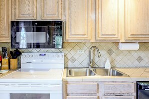 A kitchen with wooden cabinets, a microwave, a stove, a sink, and a decorative backsplash. - 1/2 Mi to Ocean! Canal-Front Key Colony Beach Home (Key Colony Beach)