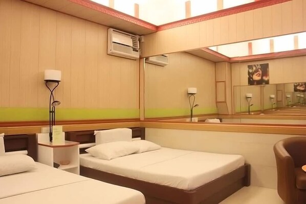 Habitación de hotel con dos camas, un espejo grande y una silla.