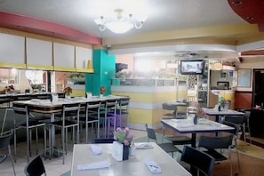 Restaurante com várias mesas e cadeiras, uma tela de televisão e um ventilador de teto.