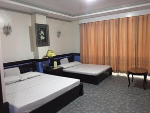 A hotel room with two beds, a nightstand, a lamp, a small table, and a window with curtains.