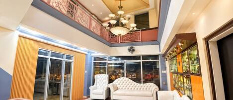 A spacious interior with a high ceiling, a chandelier, and a balcony with decorative railings.