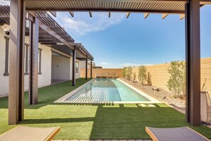 Piscina com pergolado, rodeada por um gramado bem cuidado e paisagem desértica.