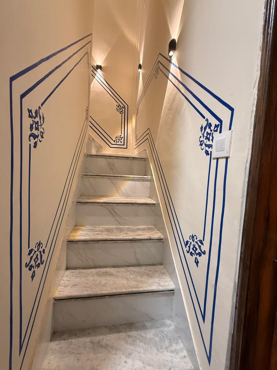 En trappa av marmor med geometriska mönster på väggarna och väggmonterad belysning.