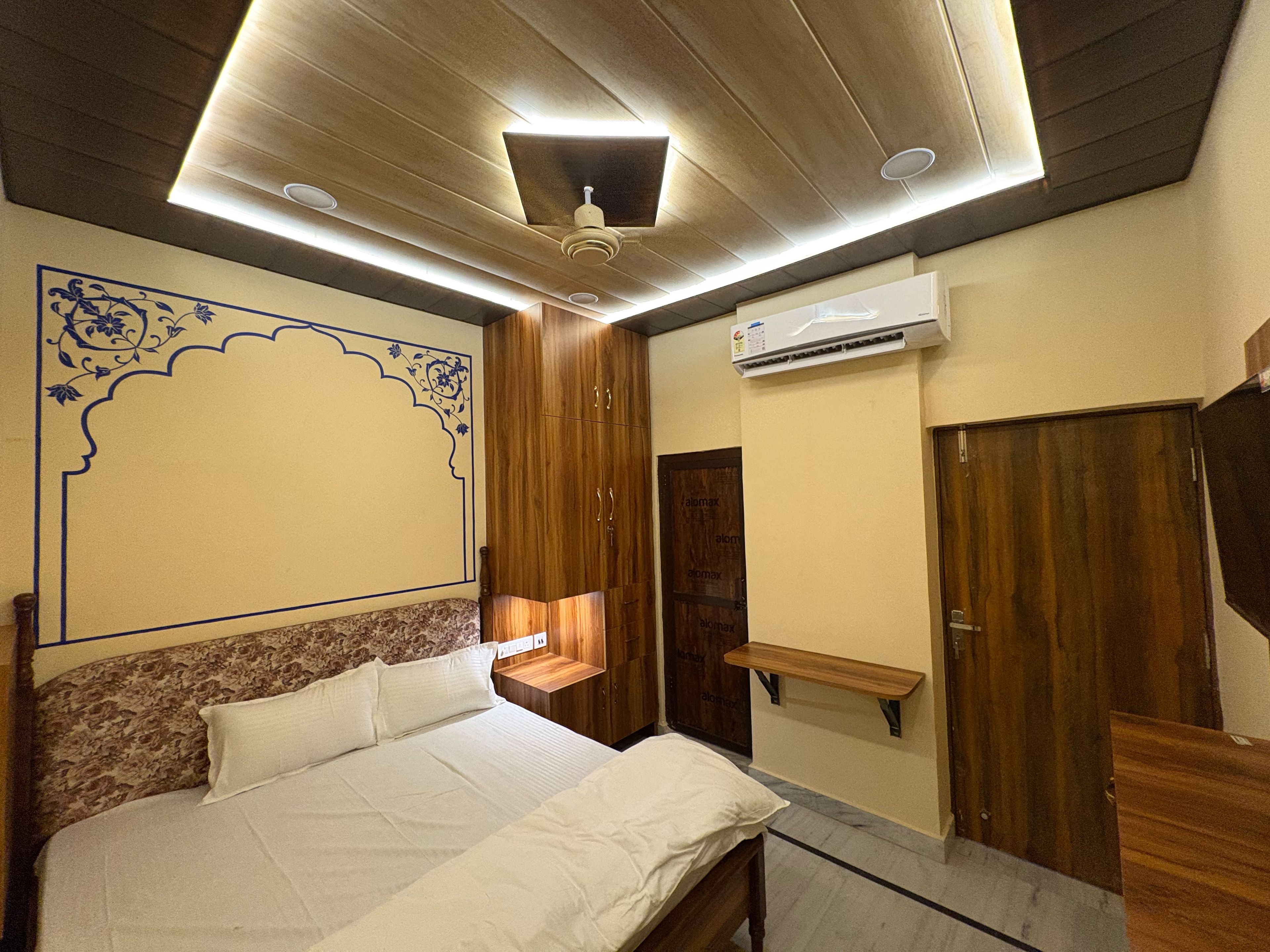 A bedroom with a bed, wooden wardrobe, an air conditioning unit, and a decorative wall design.