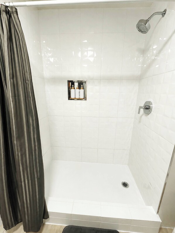 A shower area with a showerhead, a drain, and a control panel with bottles.