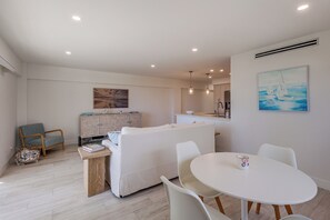 A modern living room with a white sofa, a dining table with chairs, and a kitchen area in the background. - 1 Block to Sand! Ocean-View Retreat w/ Pool Access (Fort Lauderdale)