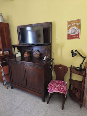 A room with a wooden cabinet, a television, a small table with a lamp, a chair, and a poster on the wall. - Old Town of Celano (Celano)