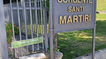 Segnaletica per Sorgente Santi Martiri, con recinzione in metallo e vegetazione sullo sfondo.