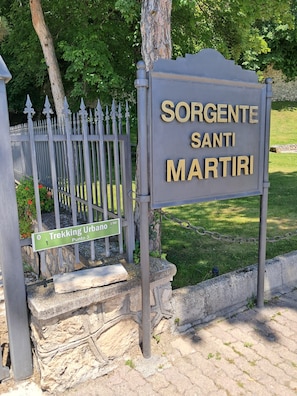 A sign for Sorgente Santi Martiri with a metal fence and greenery in the background. - Old Town of Celano (Celano)