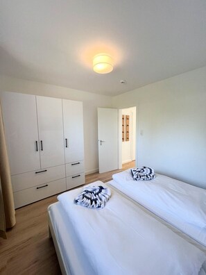 Ein Zimmer mit zwei Betten, einem Kleiderschrank und einer Tür zu einem weiteren Raum.