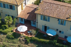 A residential building with a tiled roof, multiple windows with shutters, and outdoor seating areas with umbrellas. - La Certaldina, Luna Apartment (Certaldo)
