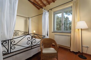 A bedroom with a four-poster bed, a wicker chair, a window with curtains, and a lamp. - La Certaldina, Luna Apartment (Certaldo)